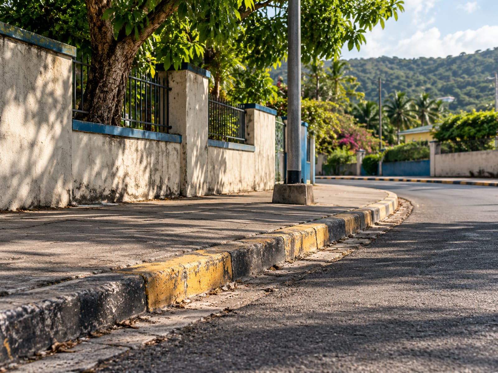 Empty painted kerb beside a lamp post and low wall on a quiet street in the afternoon with long shadows