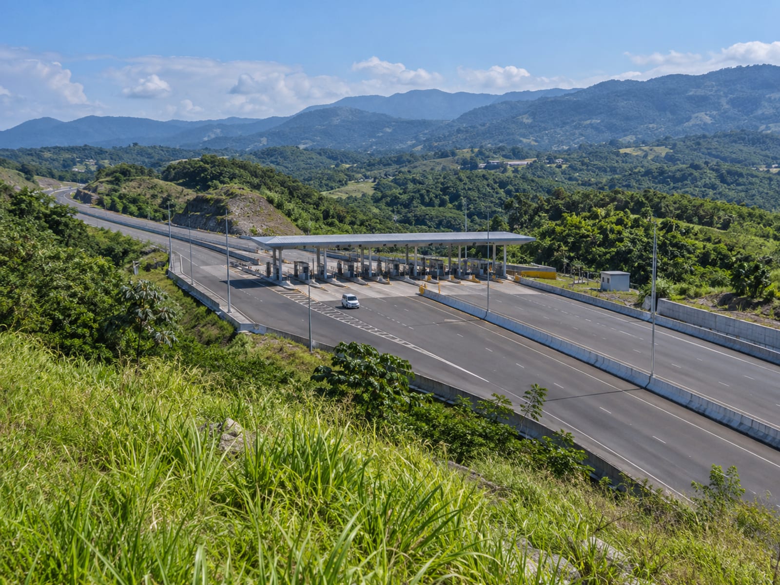 Distant stretch of toll highway with a toll plaza canopy and hills behind