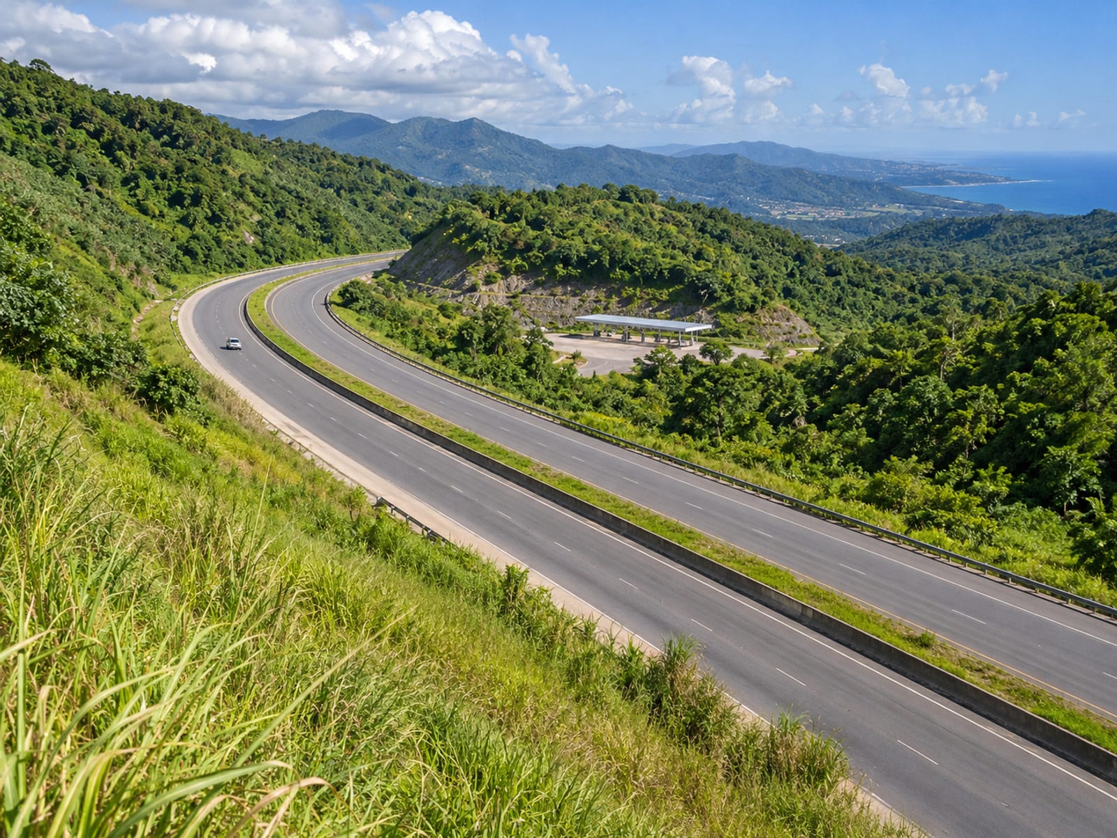 Distant view of a highway through green hills with a small roadside fuel canopy far away