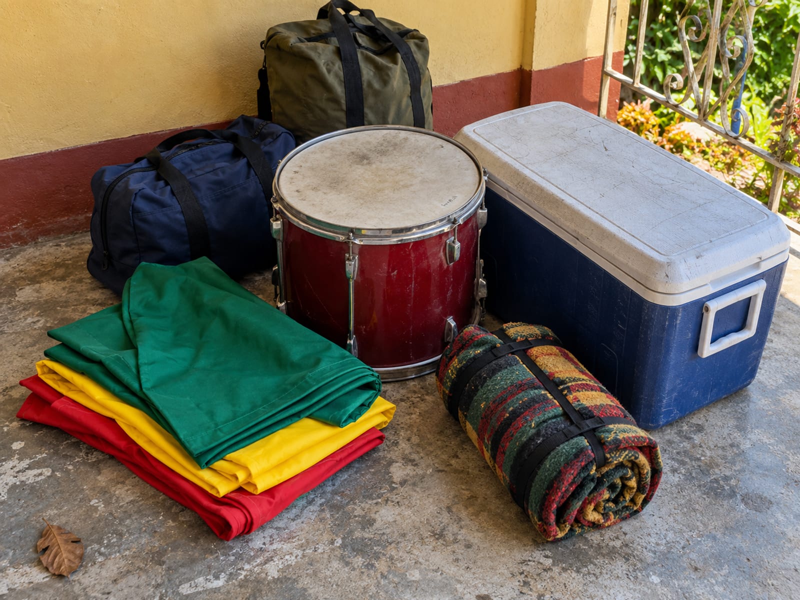 Folded plain cloth banners, a drum, a cooler box and two canvas bags resting on a concrete verandah floor