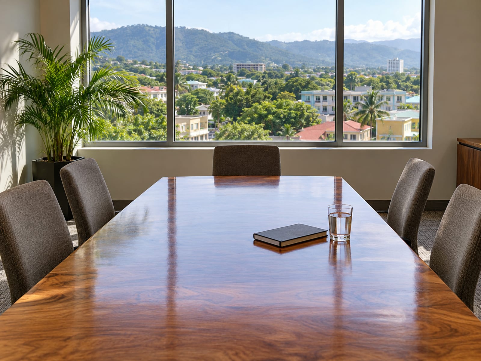 An empty meeting table with six chairs in a bright room, with a window showing low rooftops and trees outside.