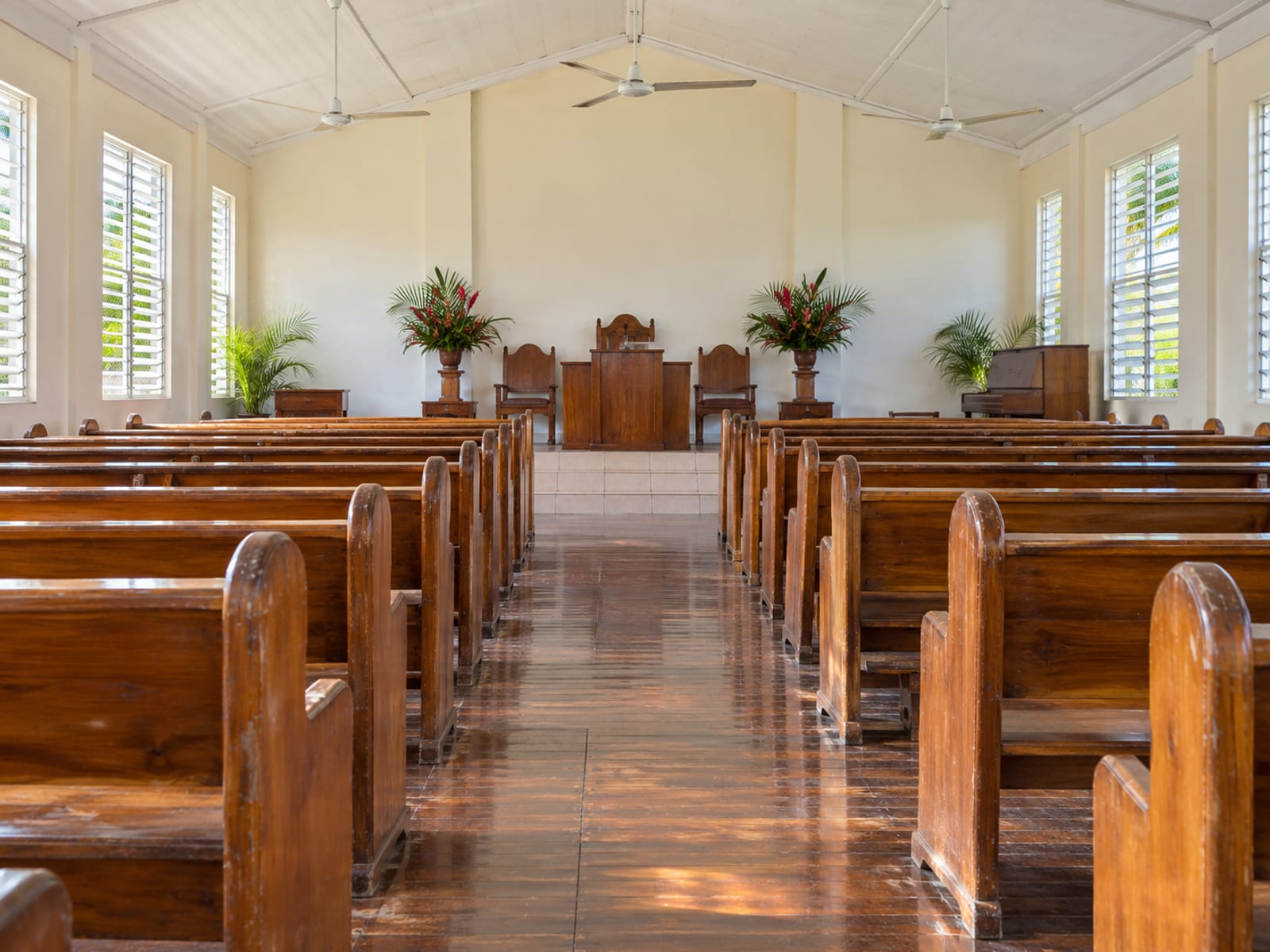 Rows of empty wooden pews with a centre aisle in a plain church lit by window light
