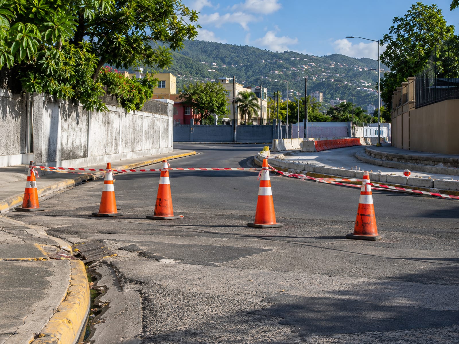 Orange cones and plain barrier tape at a closed street corner with hills behind