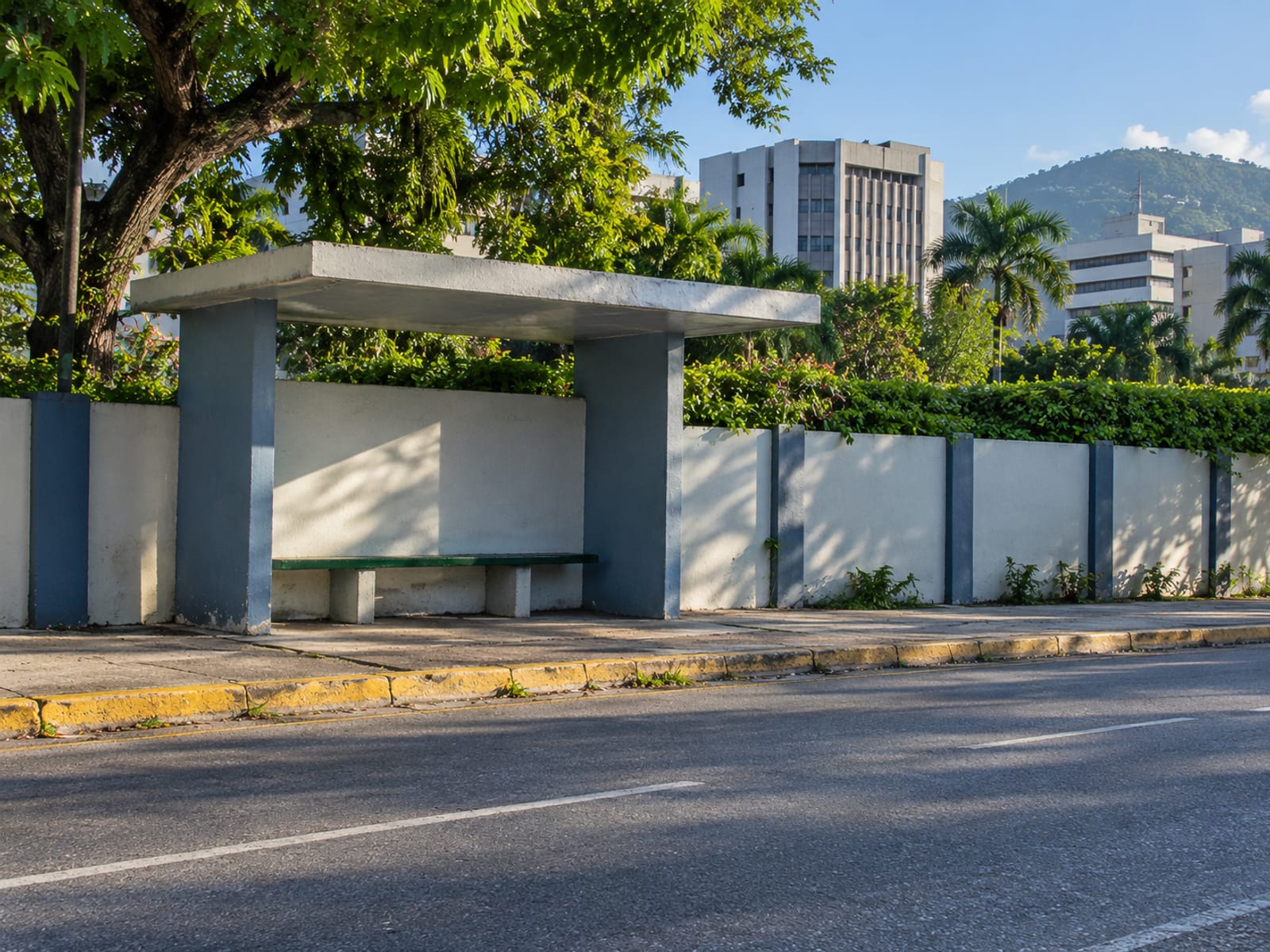 Empty plain concrete roadside shelter with a bench in front of an office park wall and a kerb
