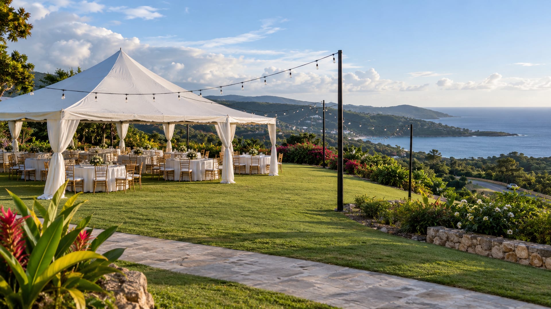 Wide view of a hillside lawn with an open tent, round tables and unlit string lights before guests arrive