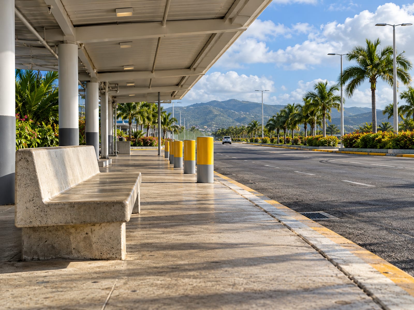 Empty covered kerbside waiting bay with a concrete bench and bollards beside a plain road in afternoon light