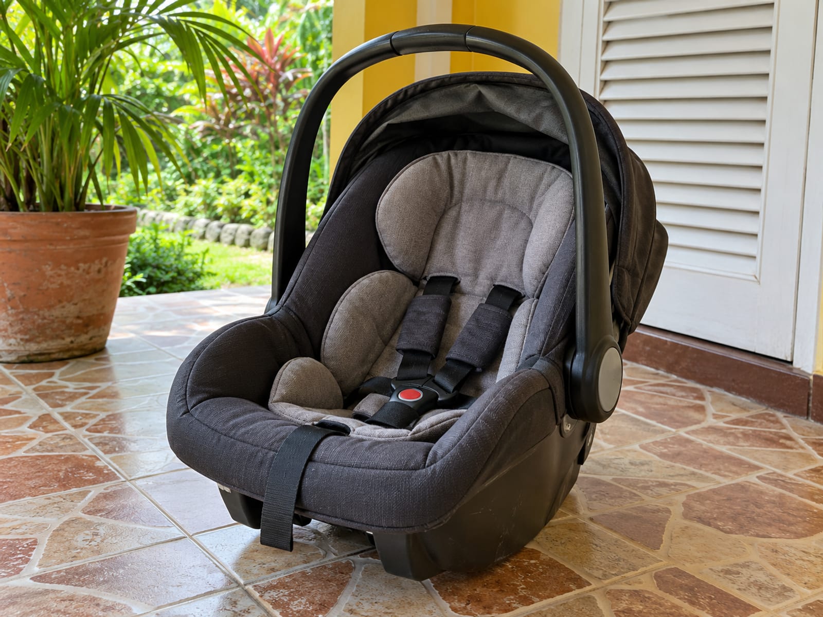 Rear facing infant car seat standing on a tiled home veranda step beside a louvre door