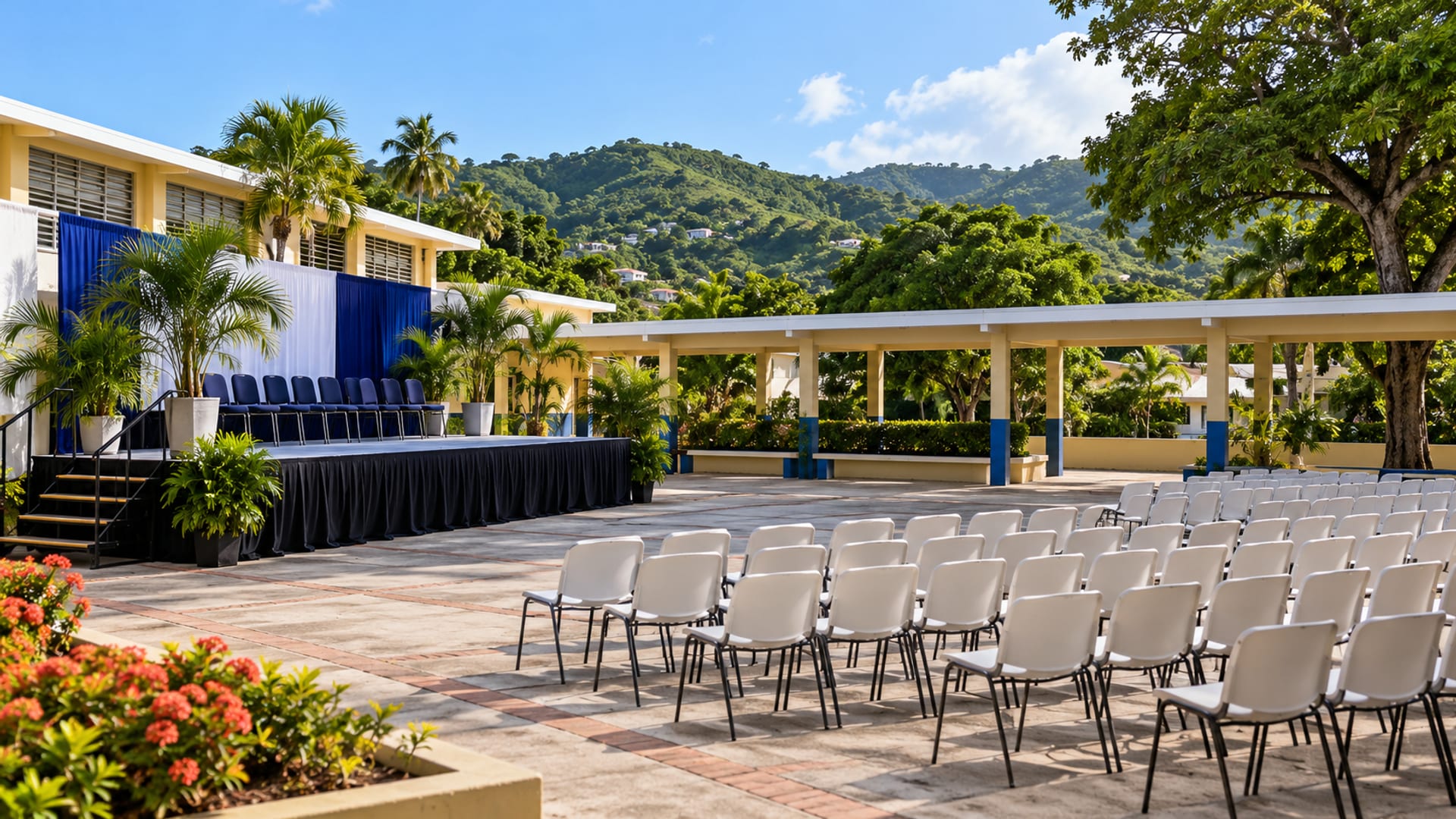 Wide view of an empty courtyard with a low stage and rows of chairs under a covered walkway, hills behind