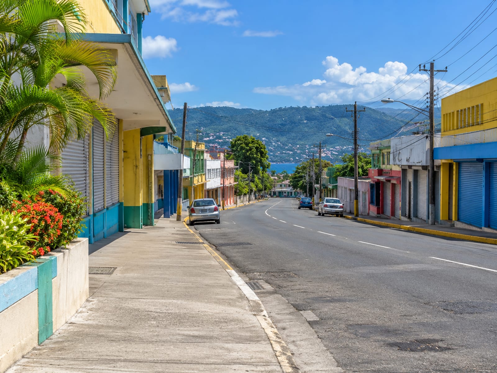 Curving town street lined with painted shops with a few tiny parked cars far down the road