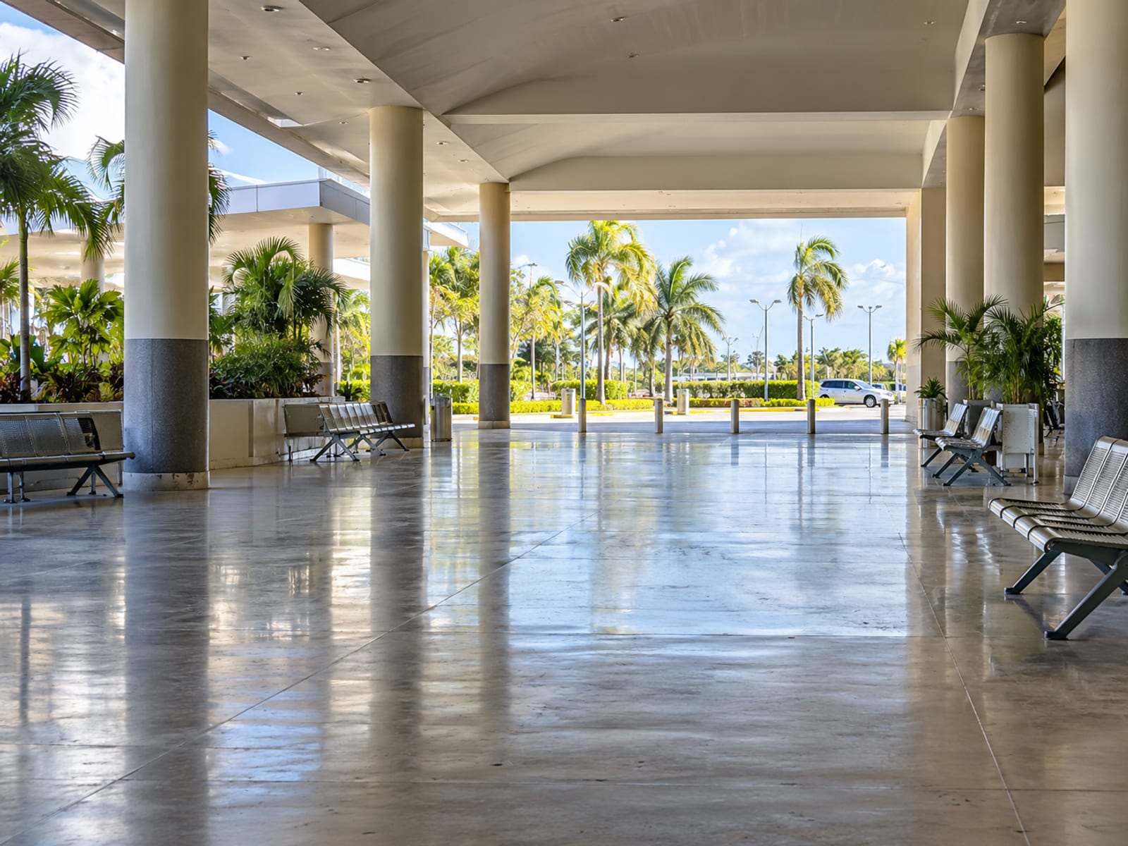 Airy open sided arrivals hall with pillars, benches and a bright exit, empty and unmarked