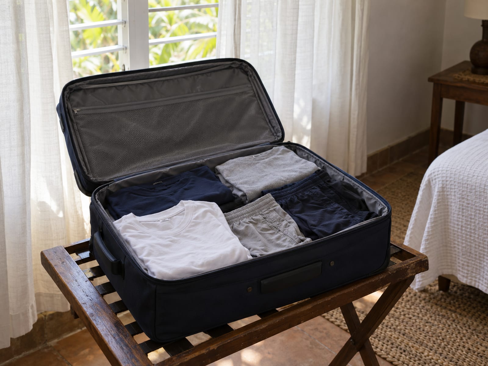Open suitcase on a luggage rack with neatly folded plain navy, grey and white clothes and no patterns