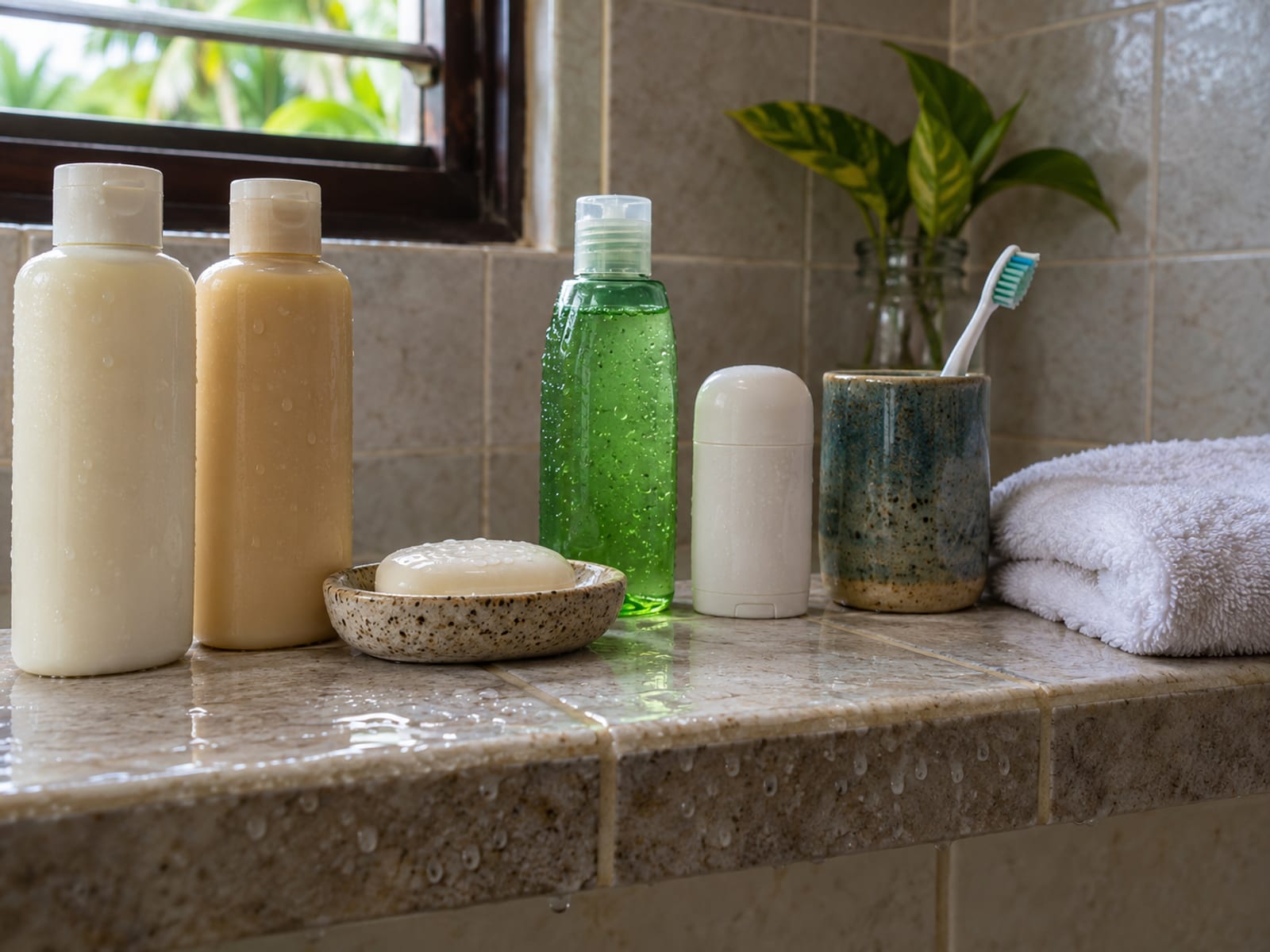 Bathroom shelf with plain unlabelled shampoo bottles, a soap bar, an aloe bottle, a deodorant stick and a toothbrush cup