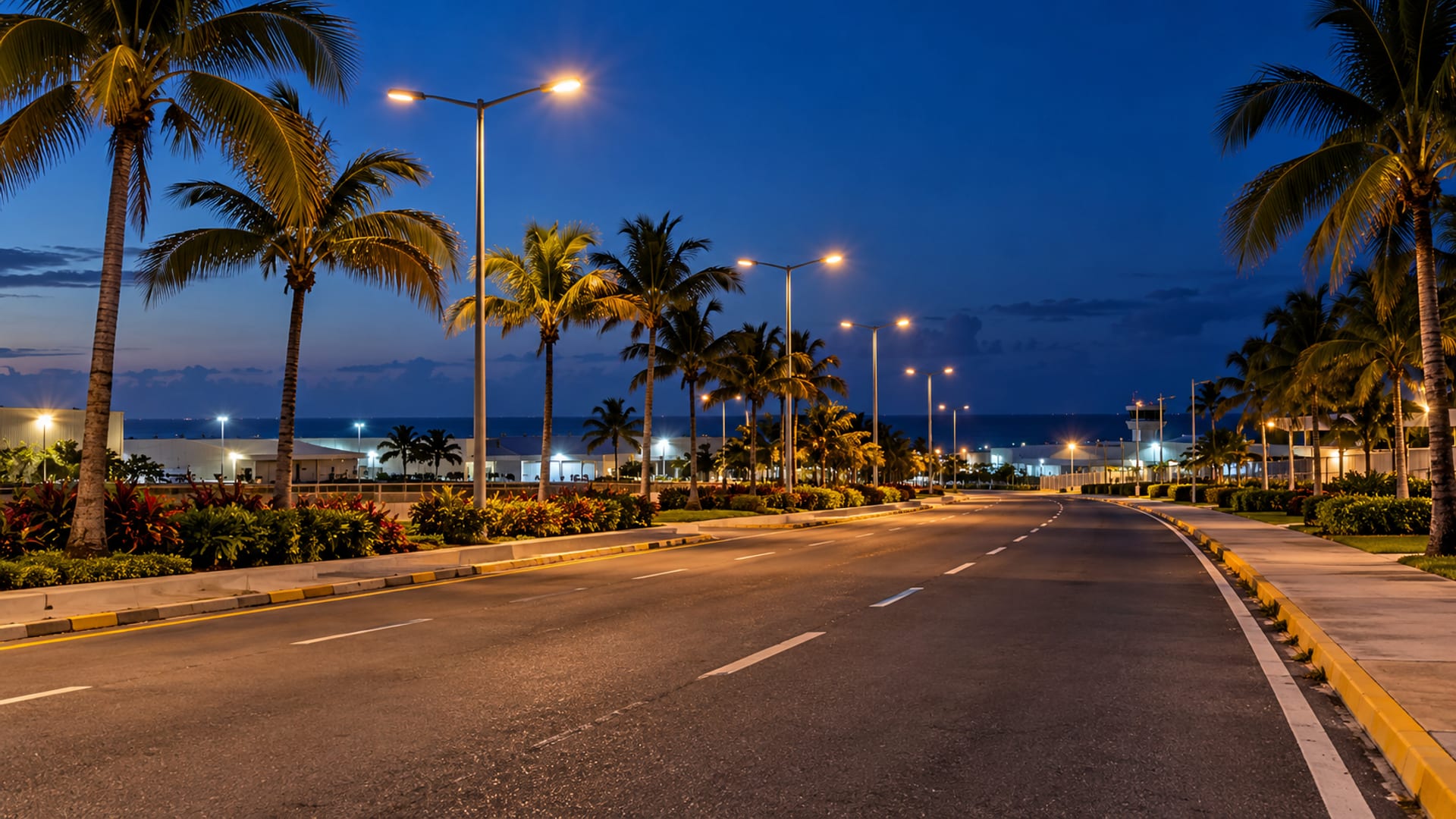 Empty airport approach road at dusk with palms lit by street lamps and a deep blue sky