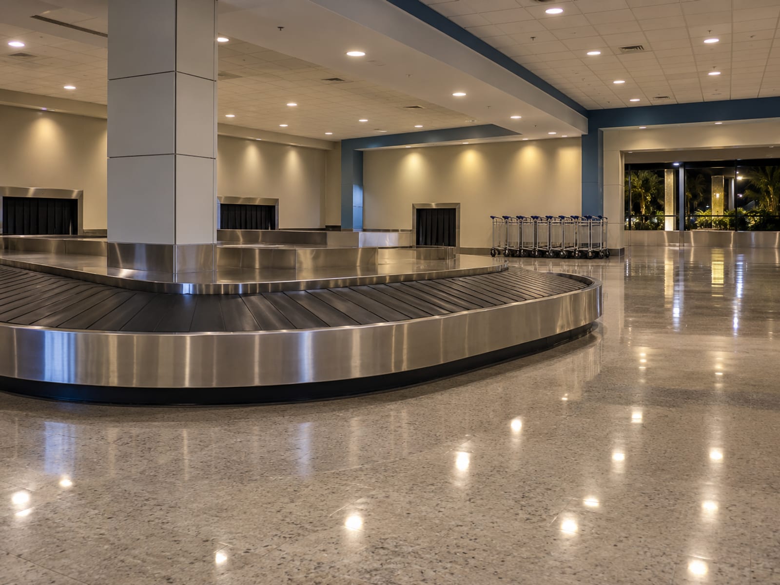 Empty baggage carousel in a quiet reclaim hall with a few luggage trolleys lined along the wall