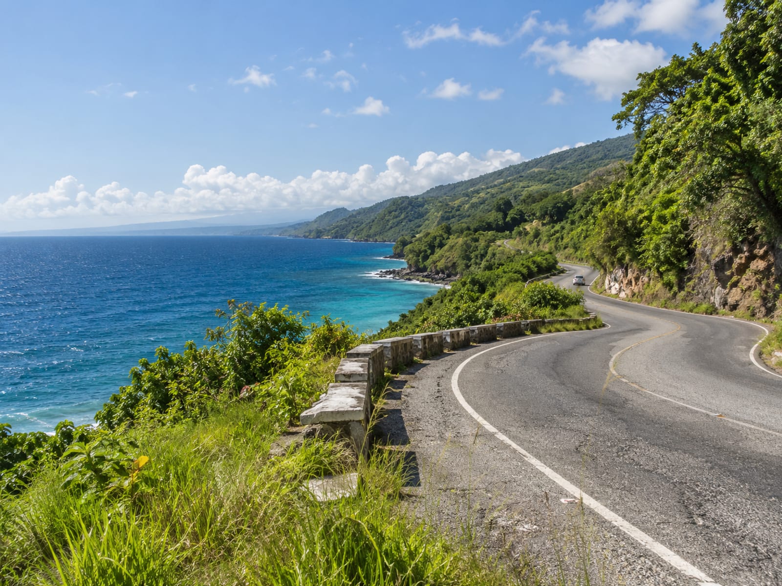 Winding two lane north coast road beside the sea with green hills and one small plain car far away