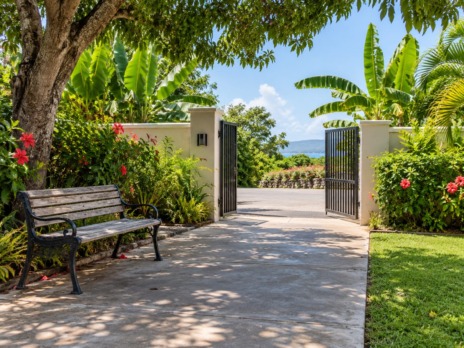 Wide view of a plain shaded bench beside a flat paved path leading to a villa gate, with garden planting either side