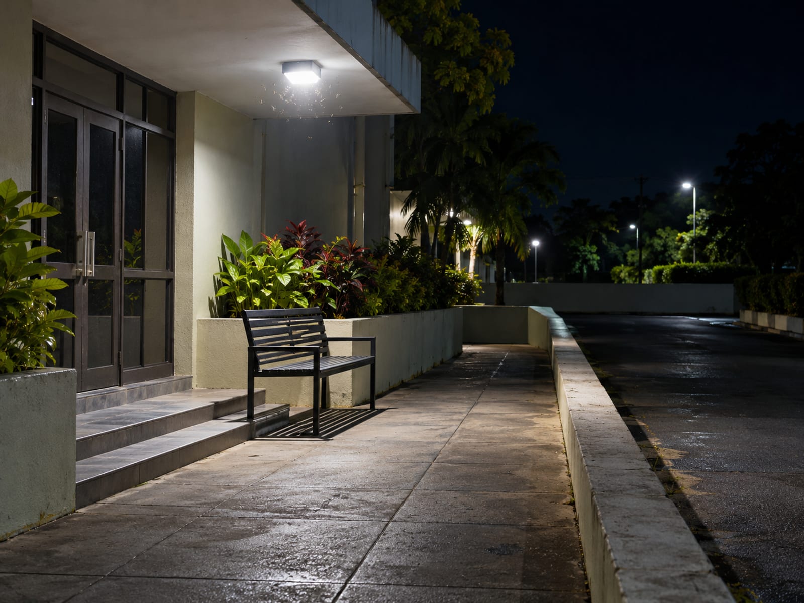 Plain bench beneath a bright security light outside a closed building entrance with a paved path