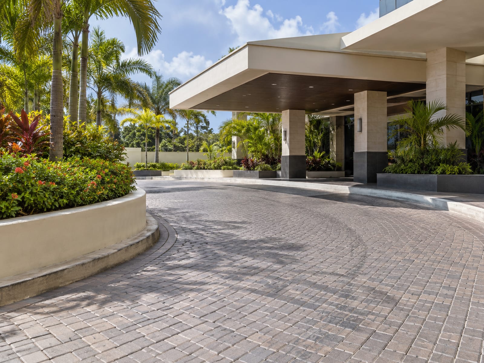 Wide curved paved forecourt and covered entrance with empty drop off area and low planters