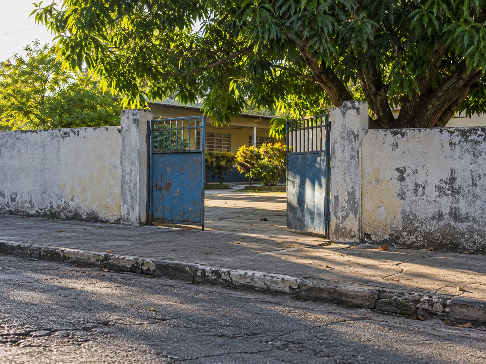 Distant open metal gate and low wall across a street in early morning with an empty pavement