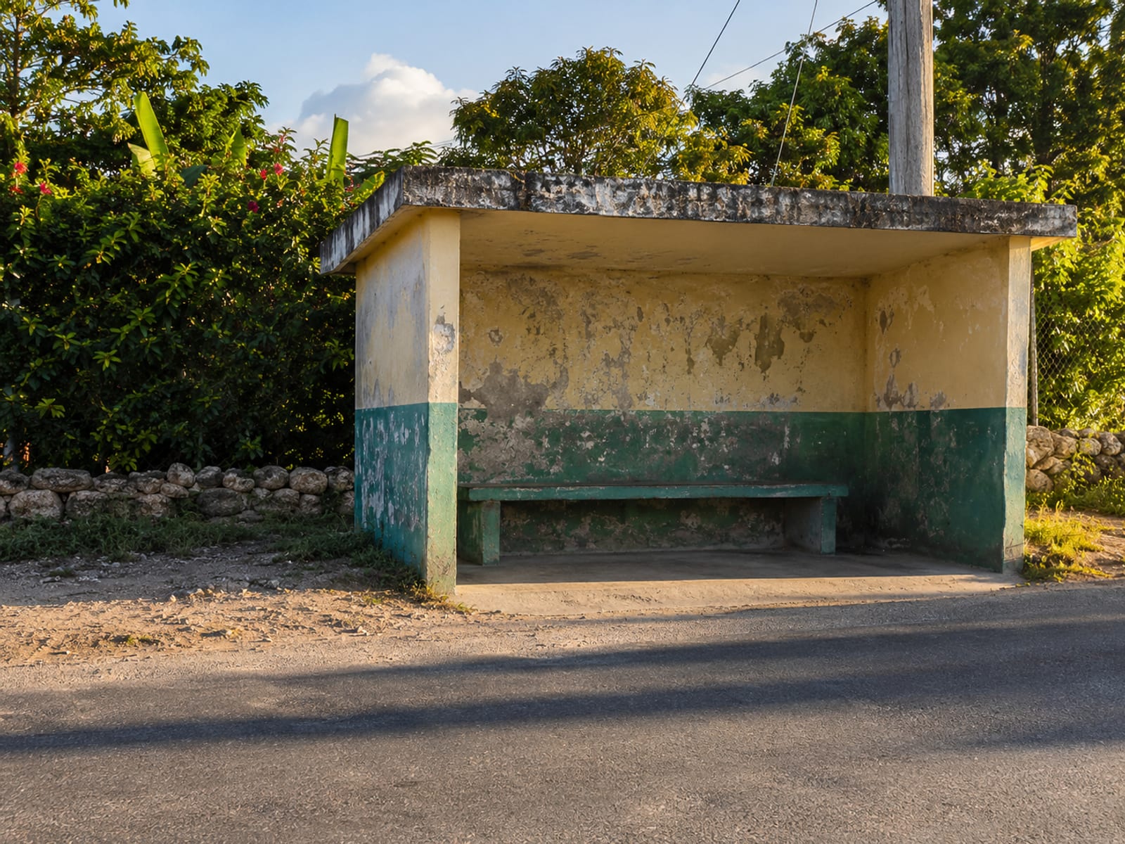 Empty roadside shelter with a bench in late afternoon, long shadows across a quiet road