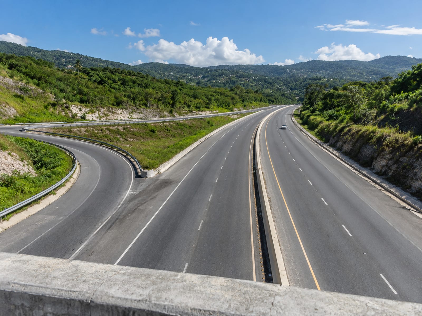 Wide highway interchange seen from an overpass with green hills and sparse traffic