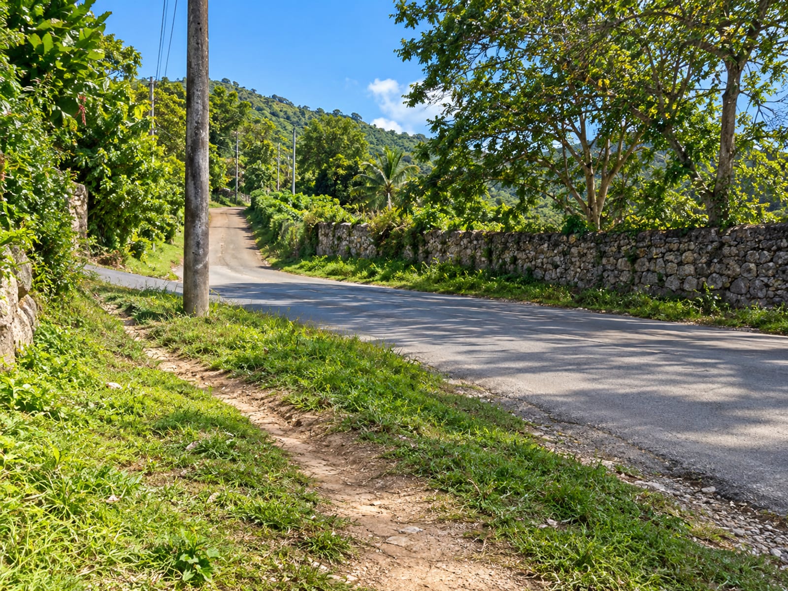 Plain roadside pole at a rural junction where a lane meets the main road, with a walking path in the grass