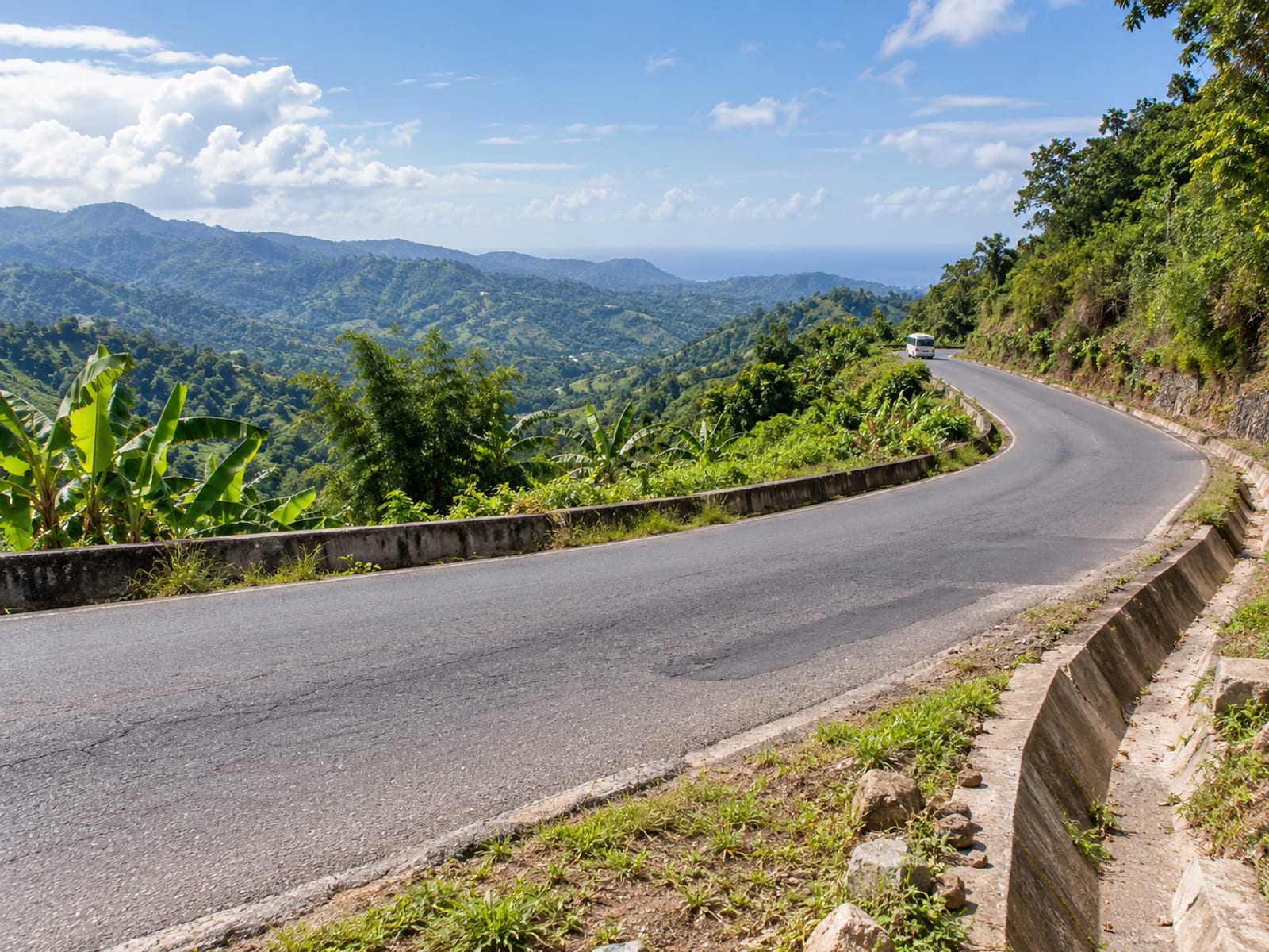 Winding country road through green hills with one small plain minibus seen very far away on a distant bend