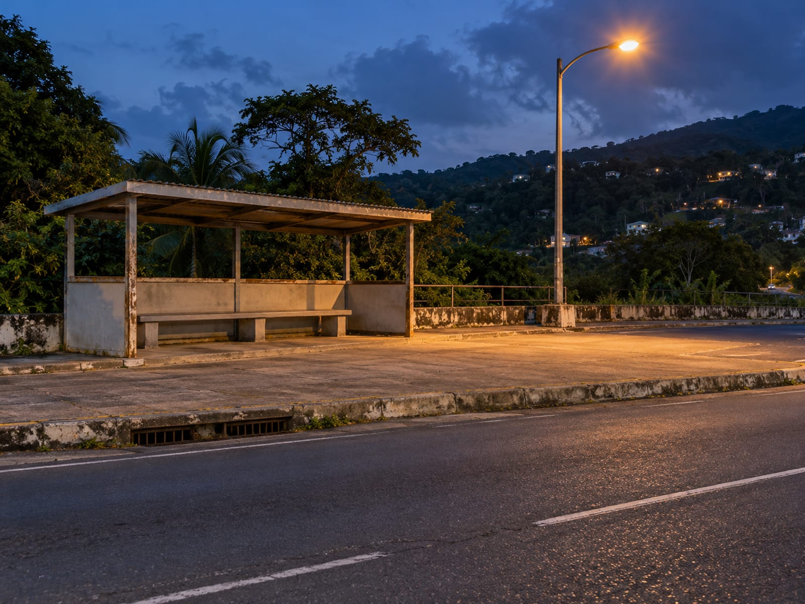 Empty covered bus shelter with a bench in a wide lay by beside a street light at dusk