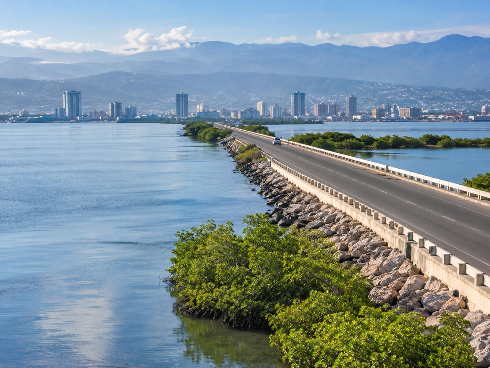 Elevated hazy view along a harbour causeway toward a distant city and blue mountains