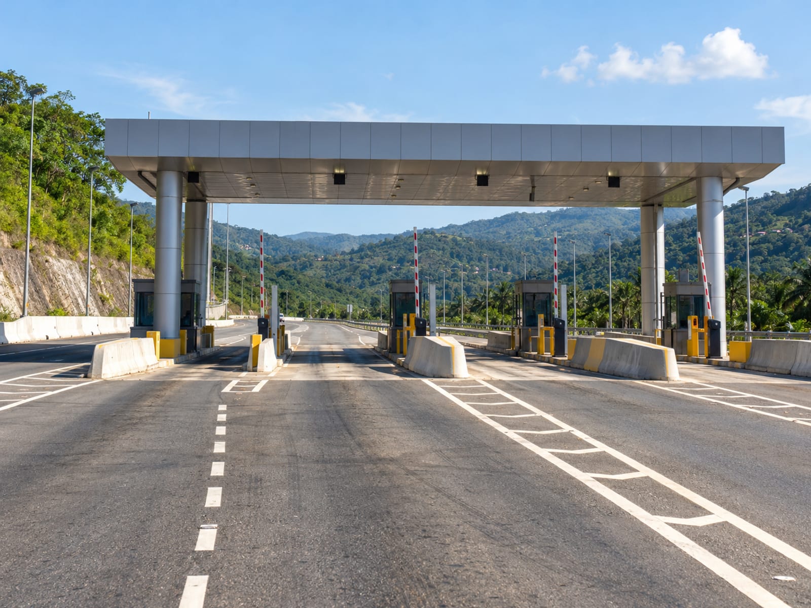 Wide multilane highway under an overhead toll canopy with empty lanes and green hills beyond