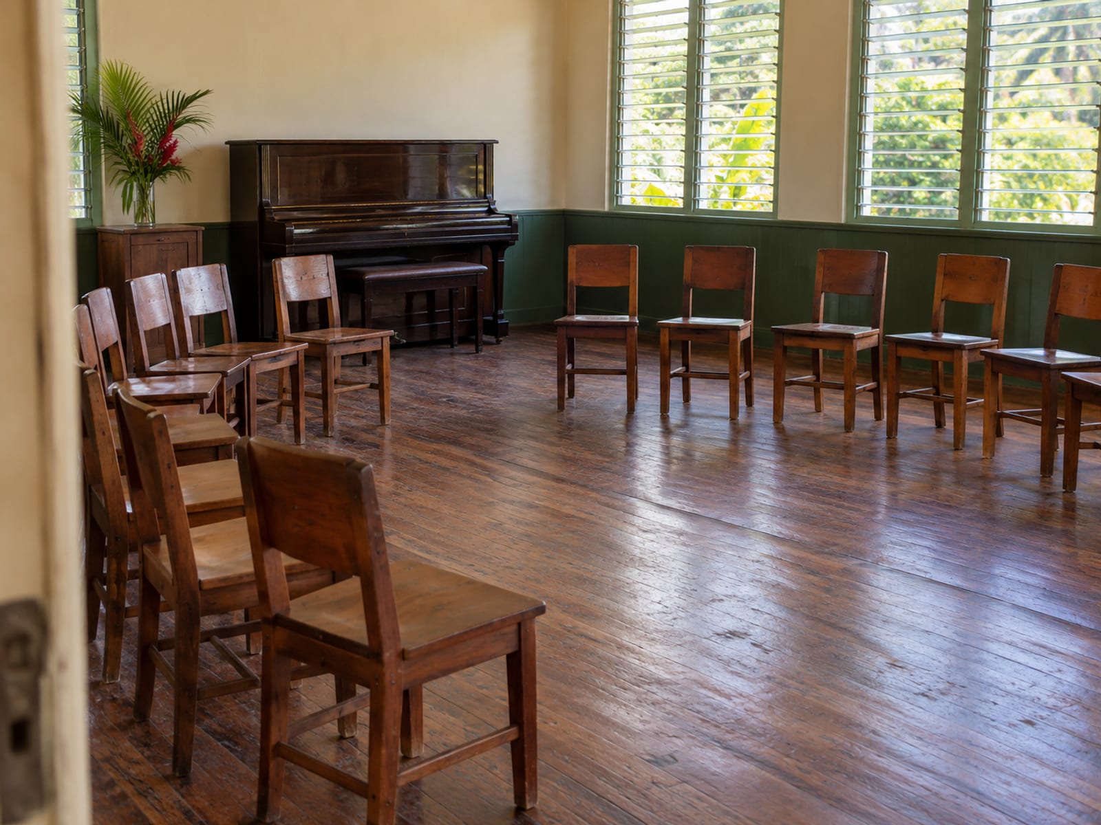 Plain hall with chairs set in a curve, a closed upright piano and windows letting in daylight.