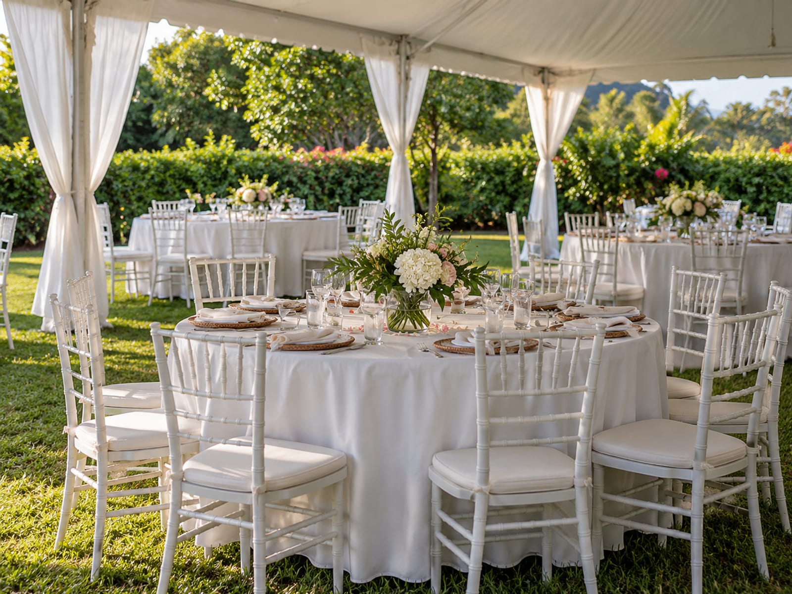 Round reception tables with plain cloths and small flower centrepieces under an open tent, empty