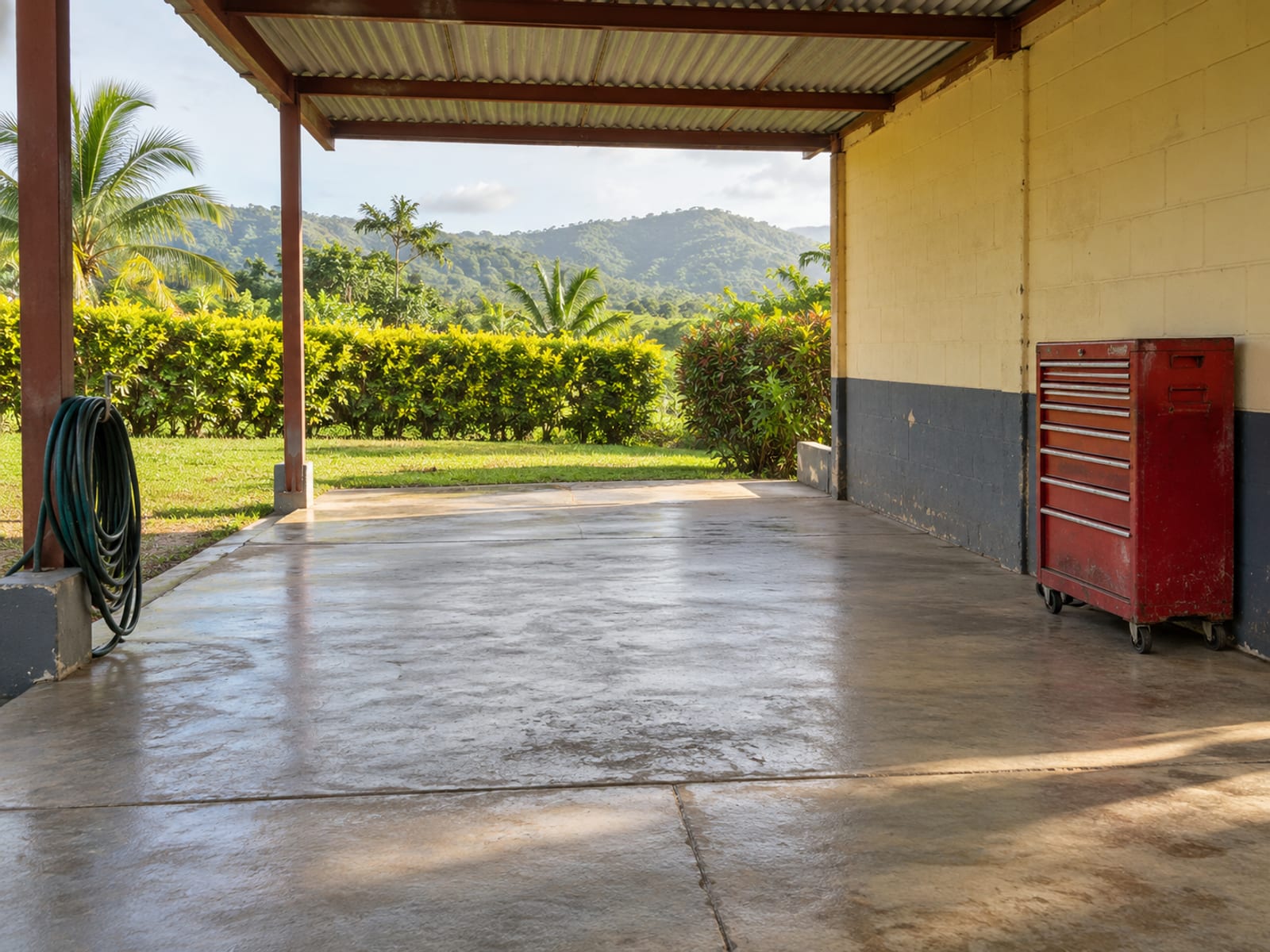 A swept, empty carport bay with a tool chest and a coiled hose