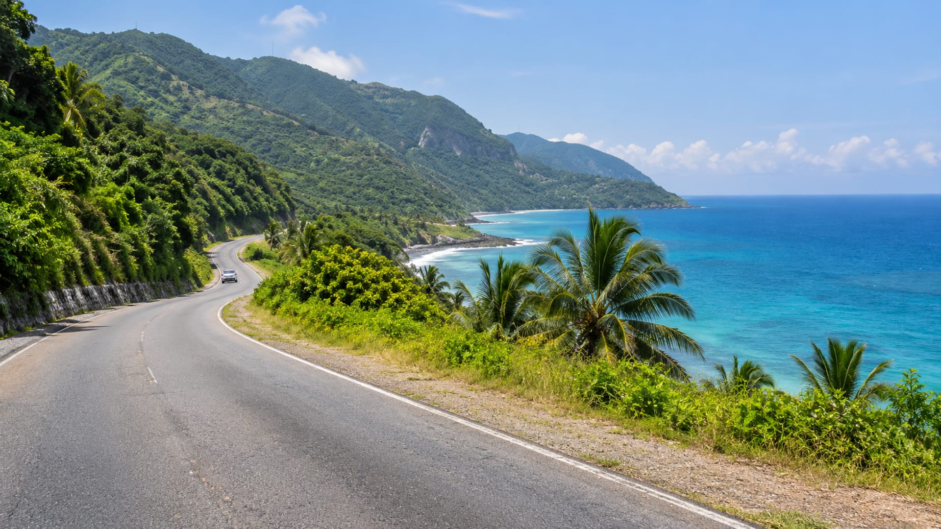 A coastal road curving between green hills and turquoise sea