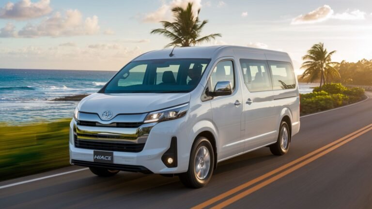 White Toyota HiAce shuttle van driving on scenic Jamaican coastal road with Caribbean Sea and palm trees at sunset